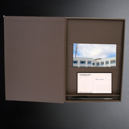 Brown open box with postcard and pen on a gray background
