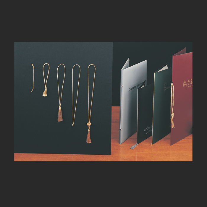 Gold tassel necklaces on a dark surface with three books in the background.