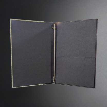 An open black binder or folder with a textured fabric cover, gold-toned metal rings, and a dark gray background.