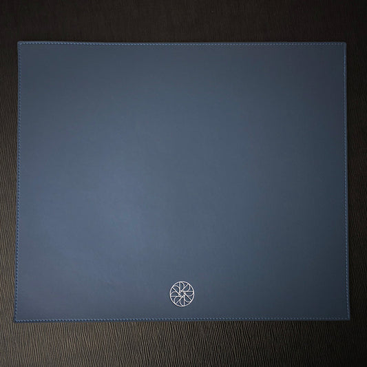A rectangular placemat with a debossed logo on the bottom right corner, on a dark background.