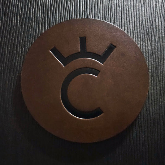 A brown leather coaster with a debossed design, placed on a wooden surface.