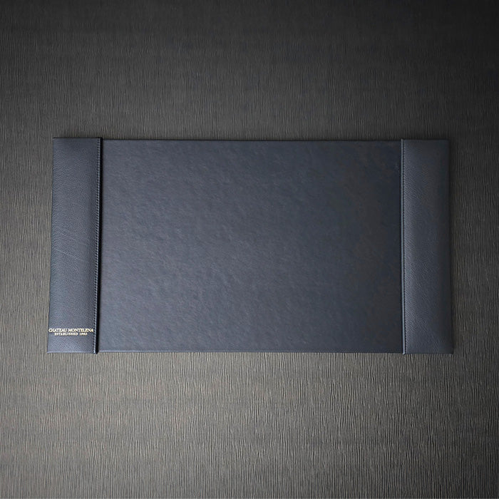 A black blotter with debossed foil decoration, turned edge construction with custom stitching, placed on a textured grey background.