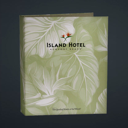 A directory binder with a green cover featuring a printed litho design with palm leaves and the text 'Island Hotel - Newport Beach'. It has a turned edge construction and a linen book cloth liner.