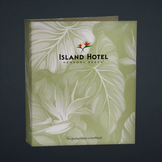 A directory binder with a green cover featuring a printed litho design with palm leaves and the text 'Island Hotel - Newport Beach'. It has a turned edge construction and a linen book cloth liner.