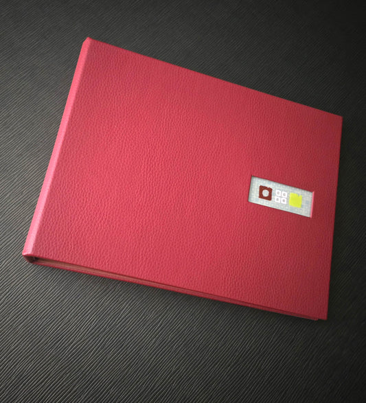 A red faux leather binder with a die cut window on the front cover for a printed acrylic tip-in, placed on a textured surface.