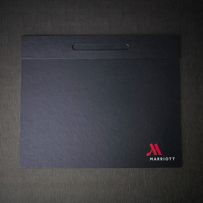 A black Marriott branded desk blotter with a pen well on the top edge.