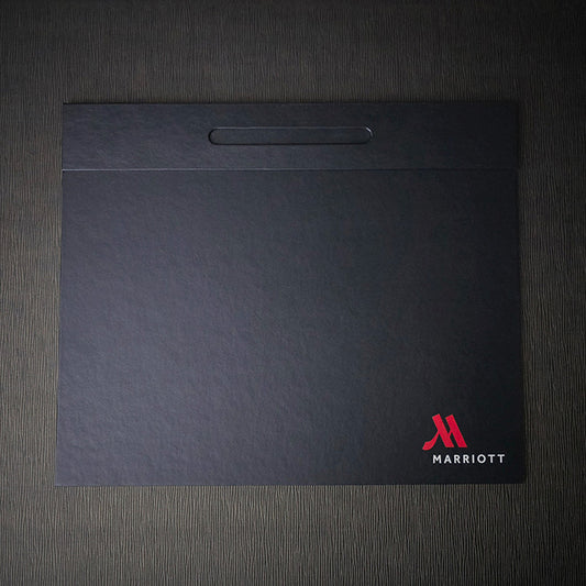 A black Marriott branded desk blotter with a pen well on the top edge.
