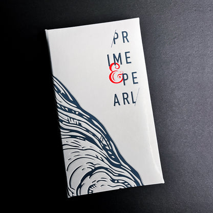 A closed white guest check with 'PRIME & PEARL' text and a decorative design in blue and gray on the cover.