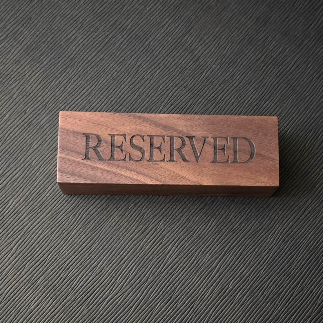 A wooden sign with the engraved text 'RESERVED' on a surface with a textured background.