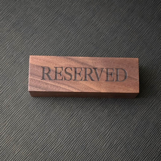 A wooden sign with the engraved text 'RESERVED' on a surface with a textured background.