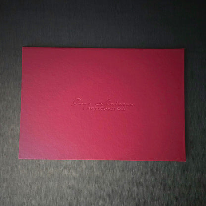 A red invitation with custom text embossed on the cover, presented on a grey background.