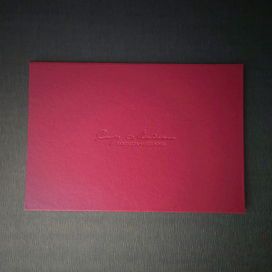 A red invitation with custom text embossed on the cover, presented on a grey background.