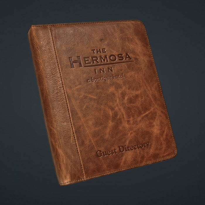 A brown genuine leather binder with the title 'THE HERMOSA INN' debossed on the cover, featuring a brass ring binder mechanism.