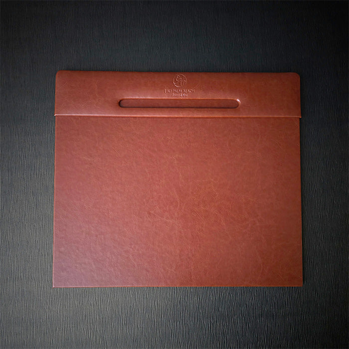 A rectangular desk blotter with Italian faux leather cover in brown, featuring a debossed logo on the top edge.