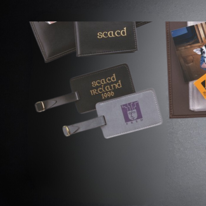 Luggage tags with 'scacd' and 'FREM' branding on a dark surface