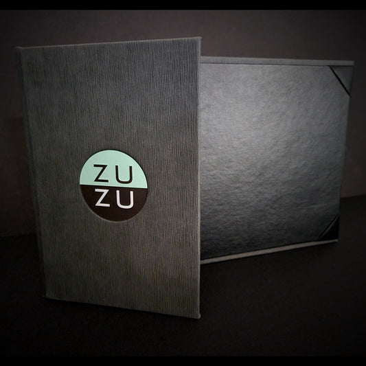 A closed pocket menu with a logo on the cover, featuring a gray Italian faux leather exterior and a black leatherette liner.