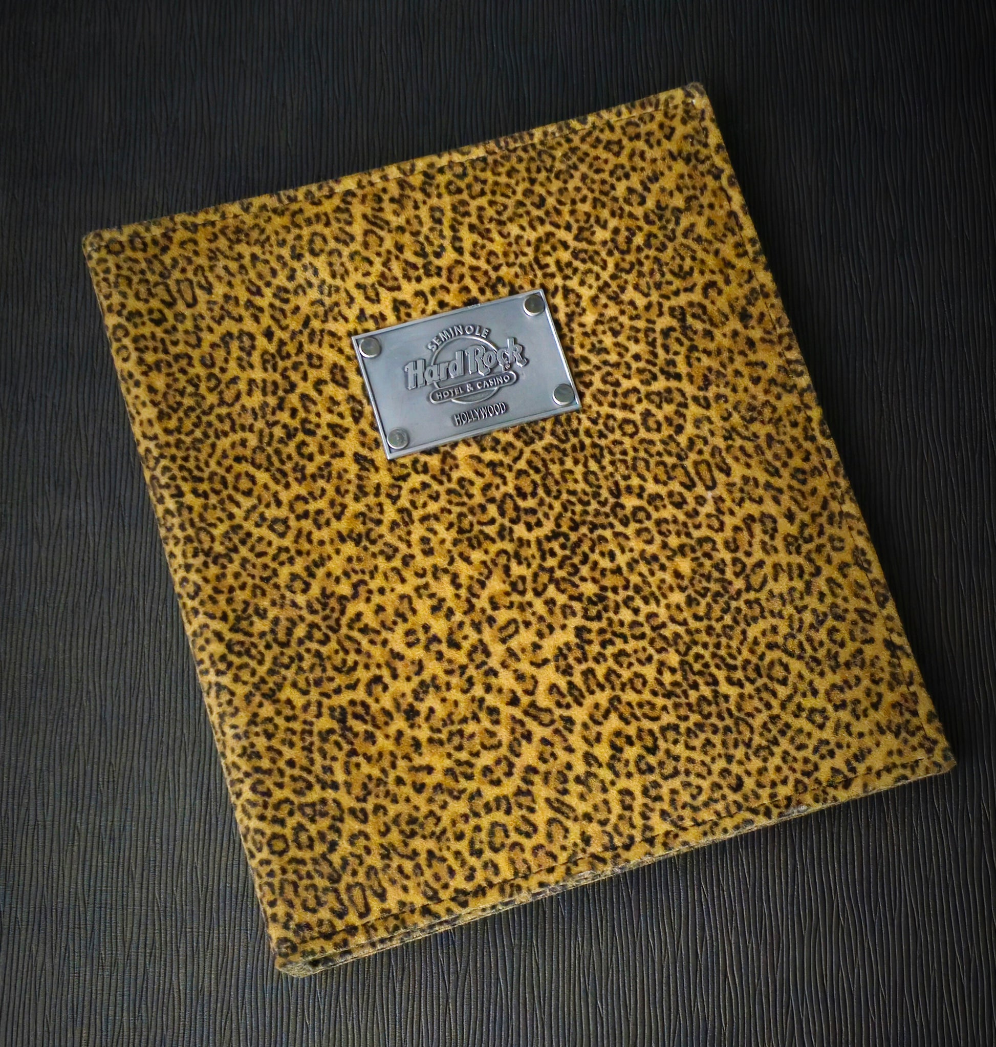 A directory binder with a faux animal fur cover featuring a leopard print pattern and a metal plate logo riveted to the front.